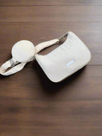 A cream-colored shoulder bag with a circular pouch lying on a wooden floor.
