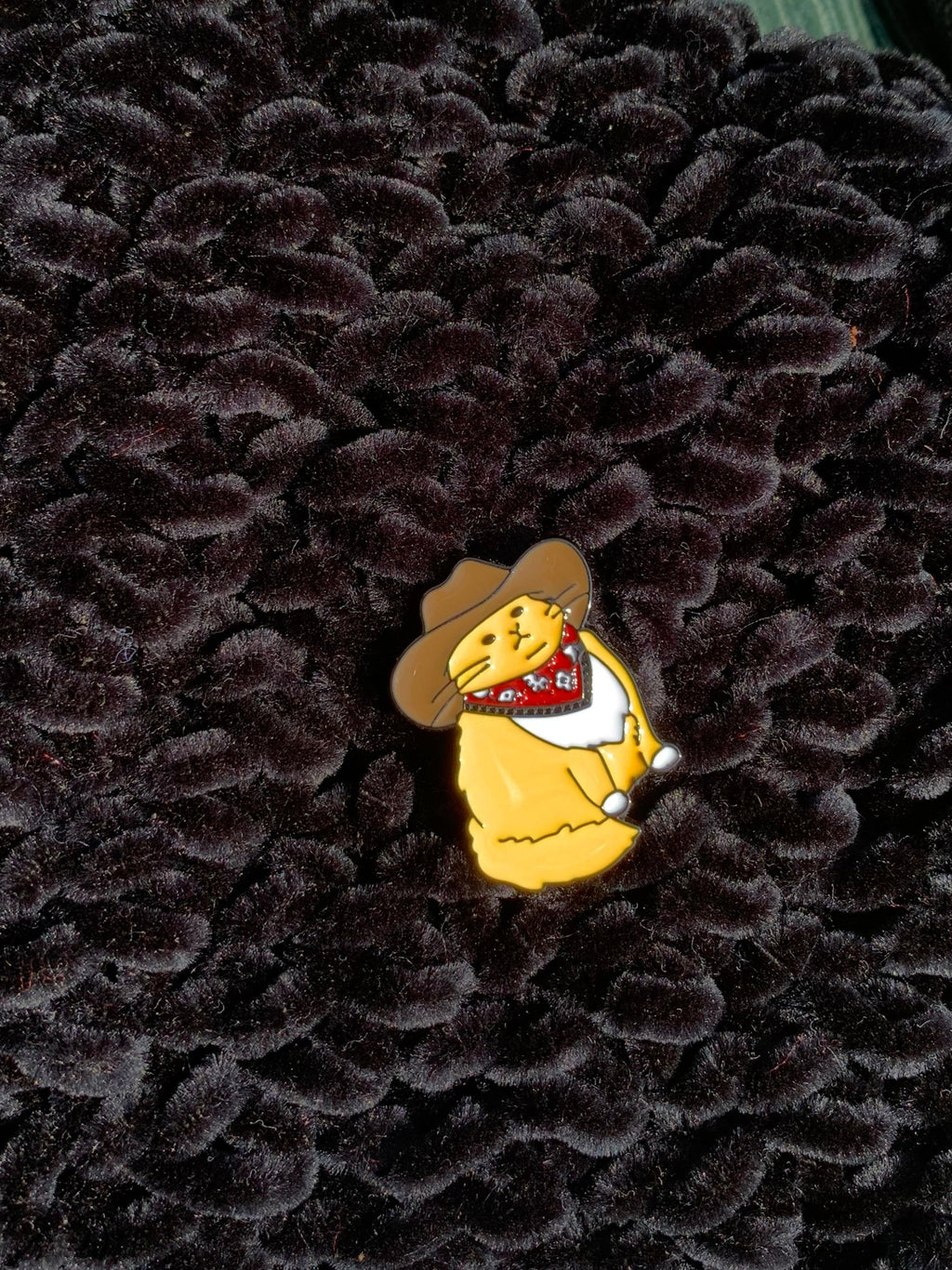 Small yellow bear pin with a cowboy hat on a textured black background