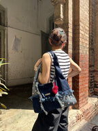 Person with a denim bag and striped shirt standing in front of a brick wall.