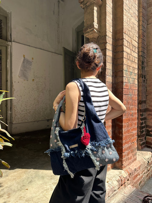 Person with a denim bag and striped shirt standing in front of a brick wall.